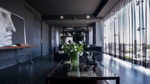A modern living room with a glass coffee table, a black sofa, and a large window with a city view.