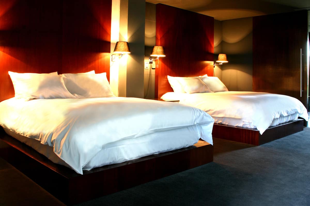 A hotel room with two beds, each with white bedding and lamps on either side.
