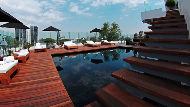 A rooftop pool area with wooden deck, lounge chairs, and umbrellas.