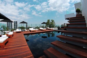 Área de piscina en la azotea con terraza de madera, sillas de descanso y sombrillas.