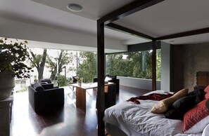 Un dormitorio moderno con una cama grande, un escritorio y una zona de estar con vistas a árboles y edificios.