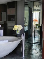 Un baño moderno con una bañera grande, un box de ducha de vidrio y un florero con flores blancas sobre una repisa.