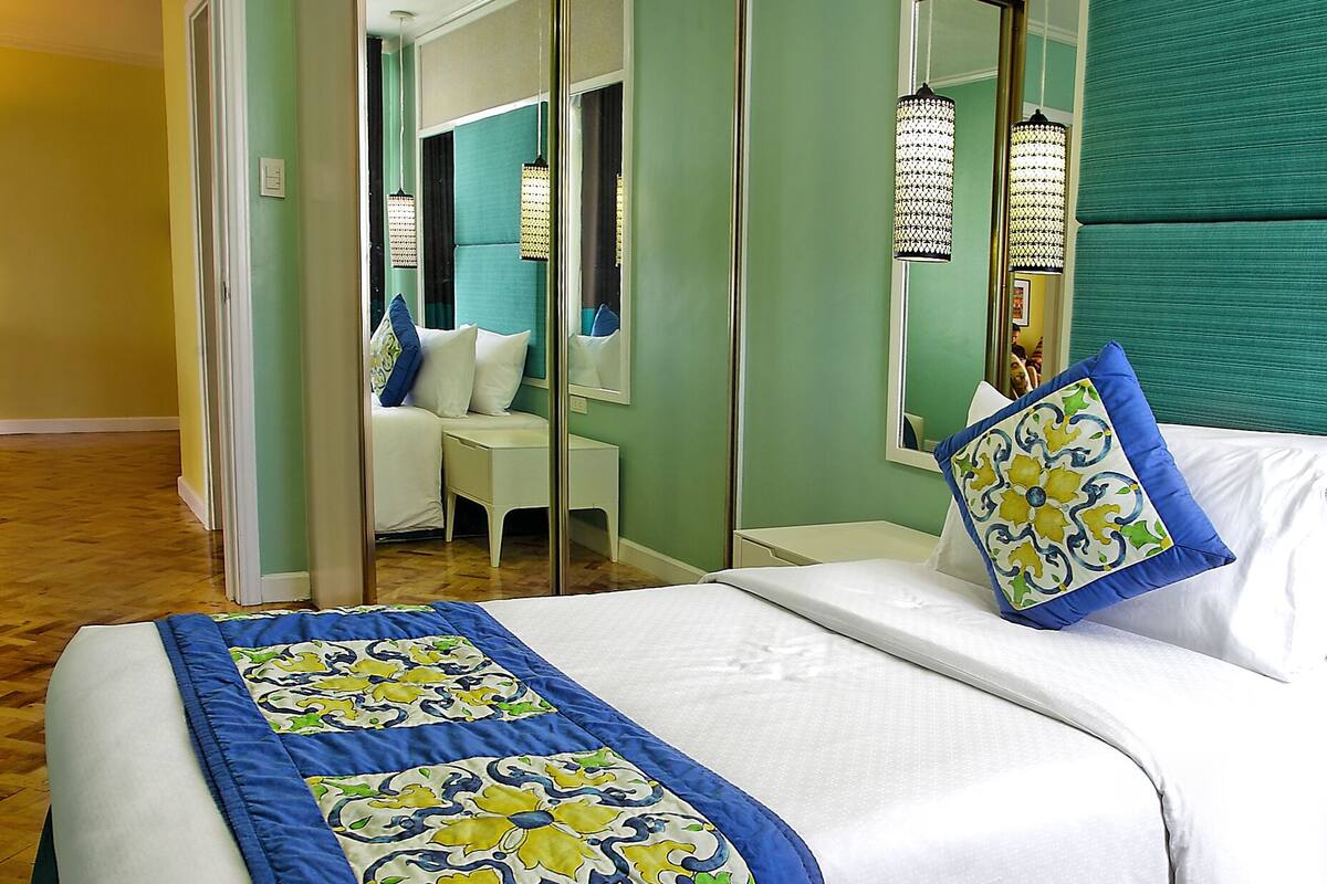 A hotel room with a bed, a mirror, and a view of the hallway.