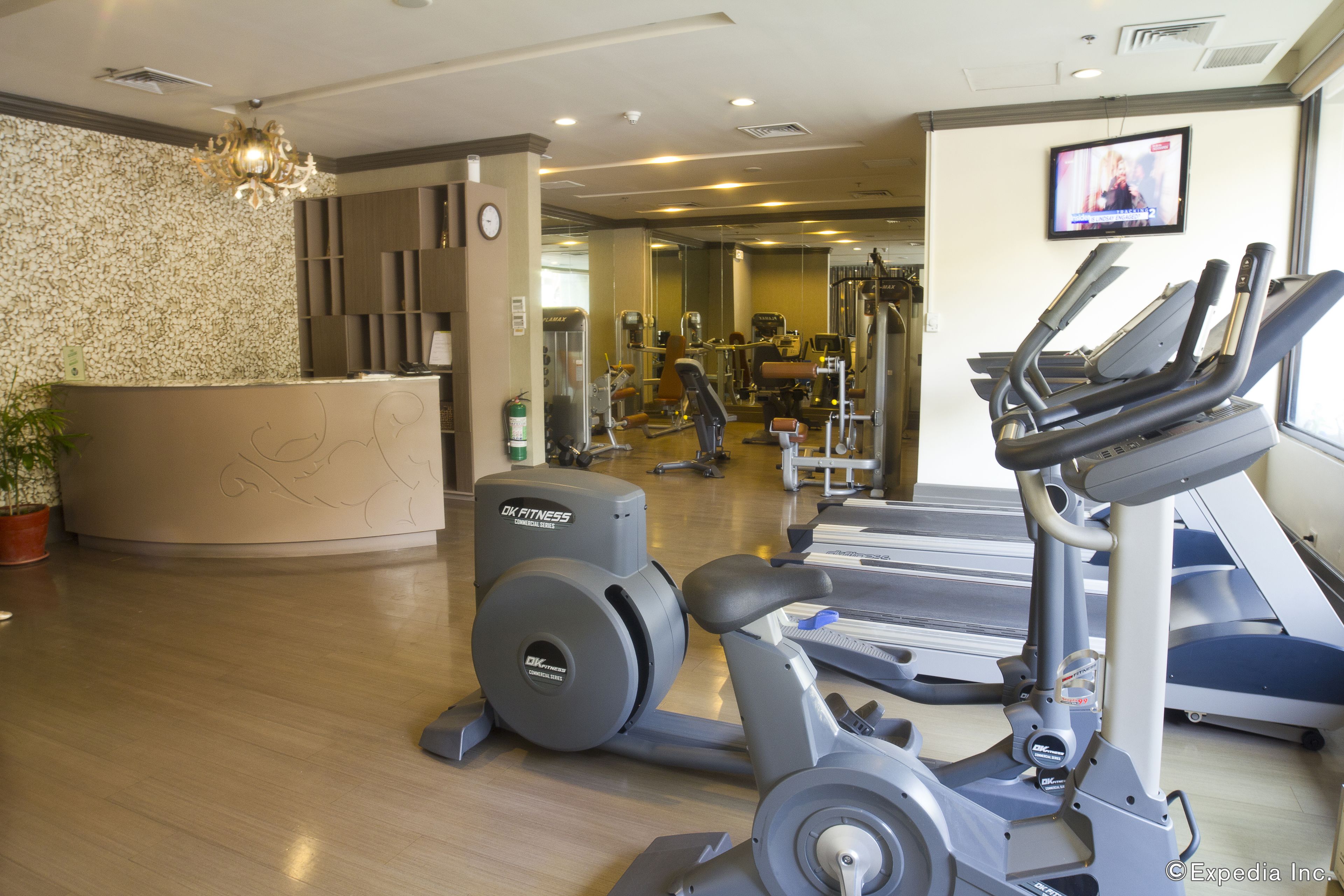 A gym with cardio equipment, a reception desk, and a TV on the wall.