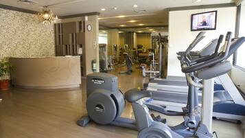 A gym with cardio equipment, a reception desk, and a TV on the wall.