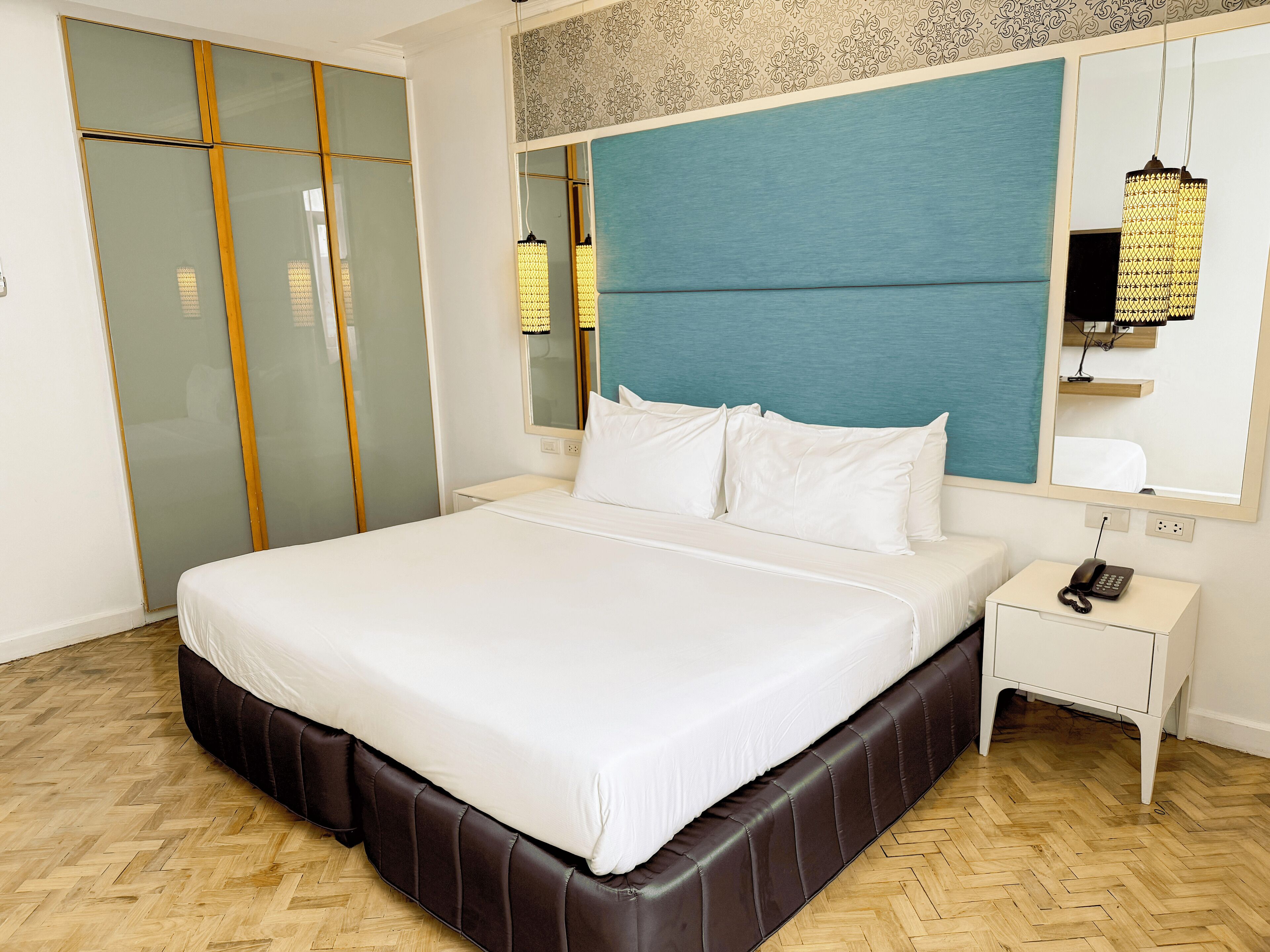 Ein Hotelzimmer mit einem großen Bett, einem Nachttisch, einem Telefon und einem Spiegel.