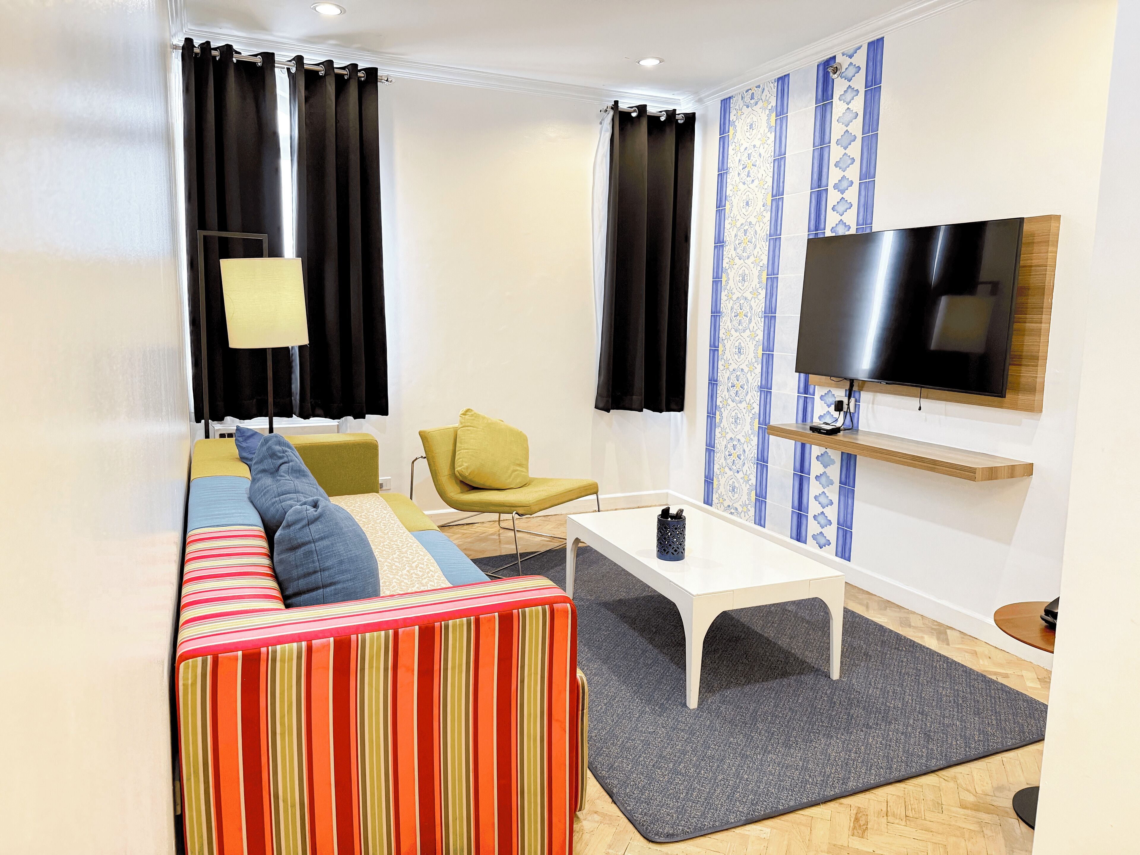 A modern living room with a sofa, a coffee table, a TV mounted on the wall, and a patterned wall.