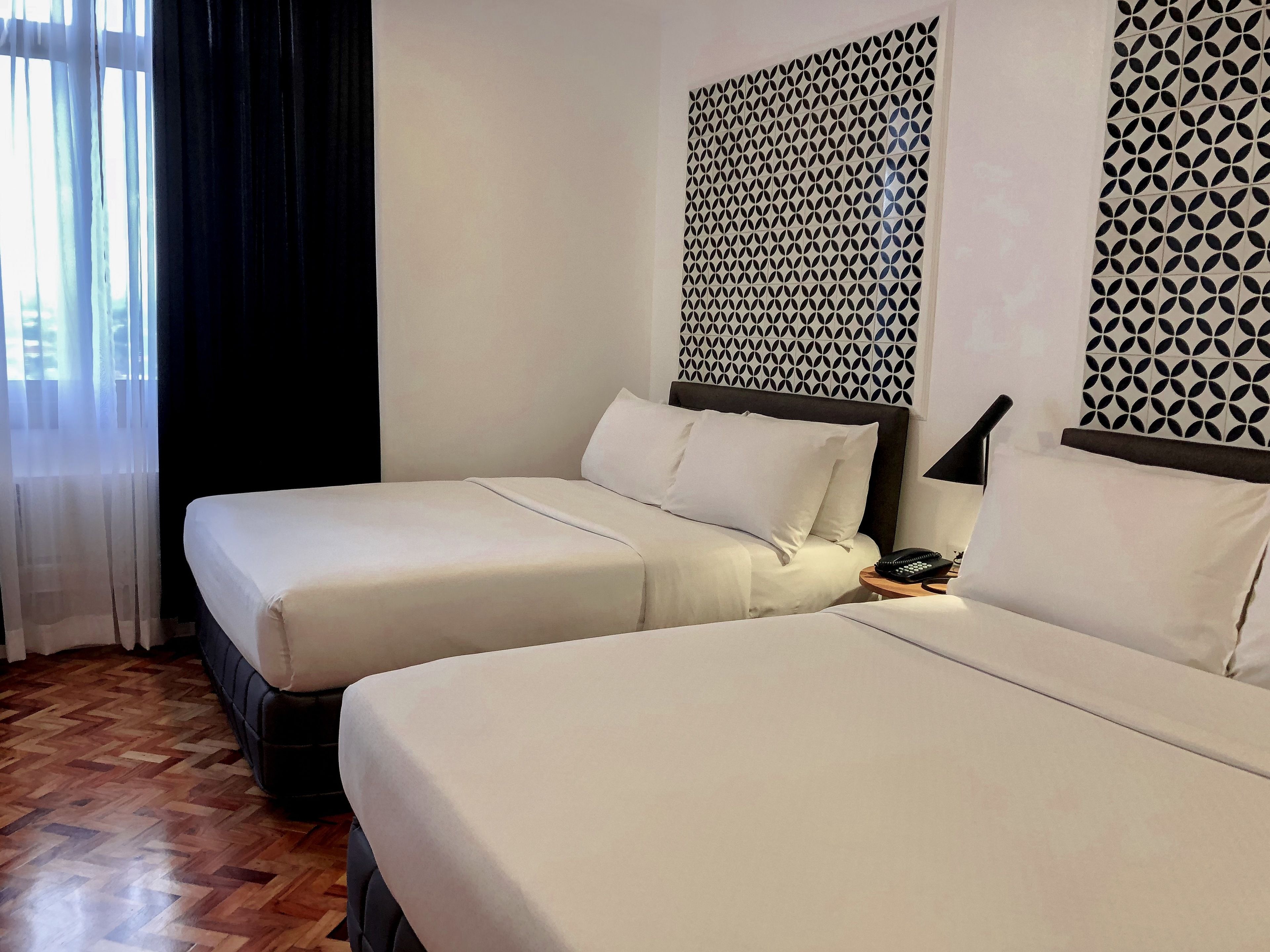 Habitación de hotel con dos camas, piso de madera, pared estampada y ventana con cortinas.