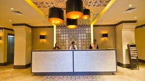 Zona de recepción con pared de baldosas estampadas, mostrador de recepción y techo decorativo.