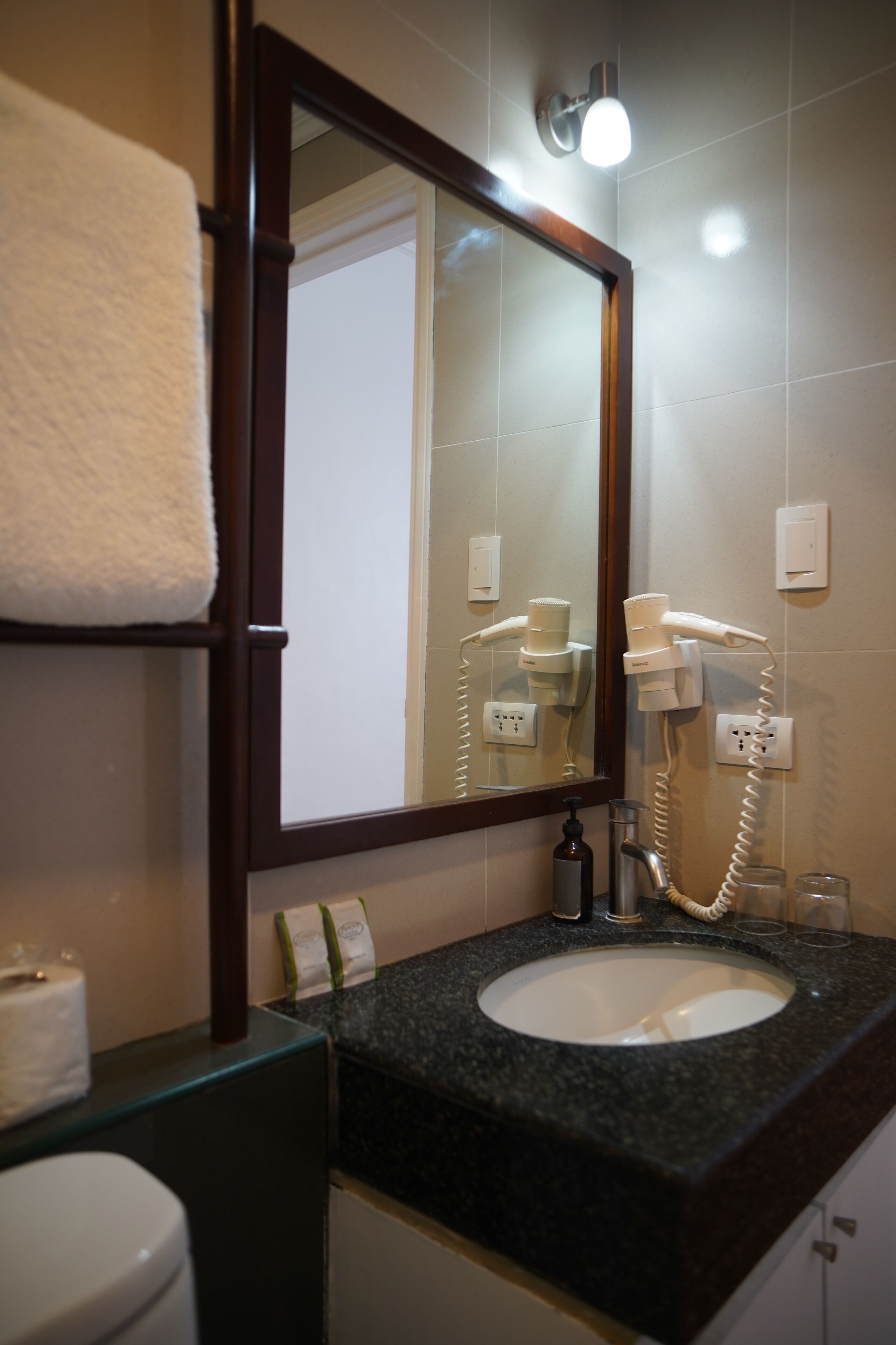 Un baño con lavamanos, espejo, secador de pelo y toallero.