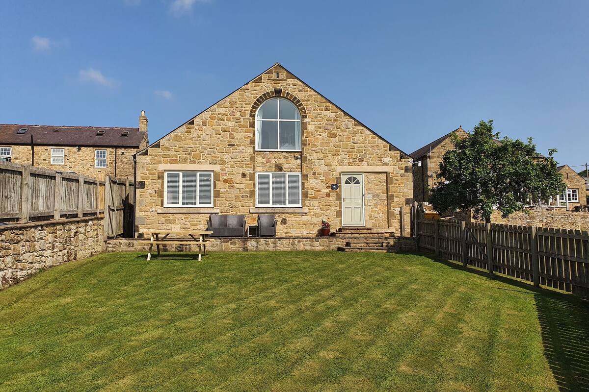 A stone house with a large window, a door, and a small patio with a bench.