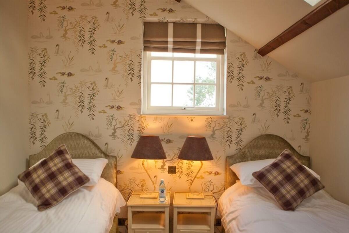 A bedroom with two beds, a window, and a nightstand with a lamp.