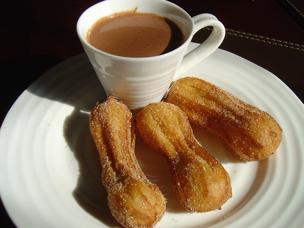 Lautasella on churroja ja kupissa kahvia.