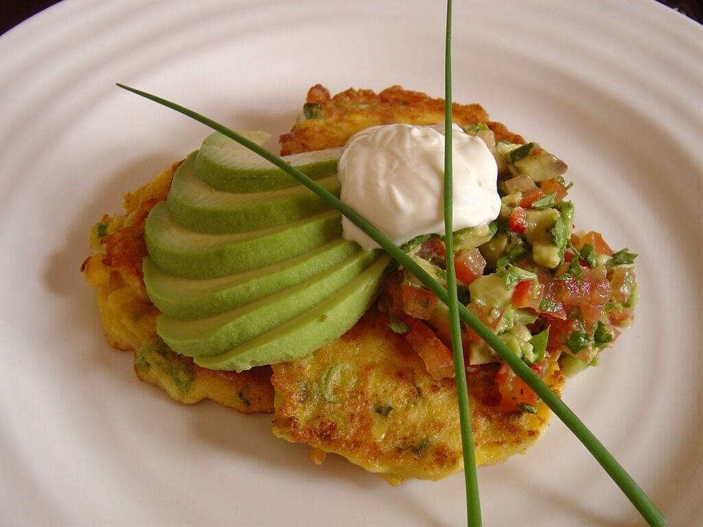 A plate with a potato pancake, avocado slices, a dollop of sour cream, and a salsa garnish.