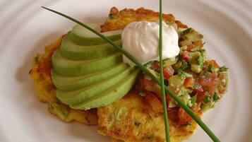 A plate with a potato pancake, avocado slices, a dollop of sour cream, and a salsa garnish.