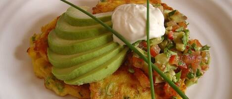 A plate with a potato pancake, avocado slices, a dollop of sour cream, and a salsa garnish.