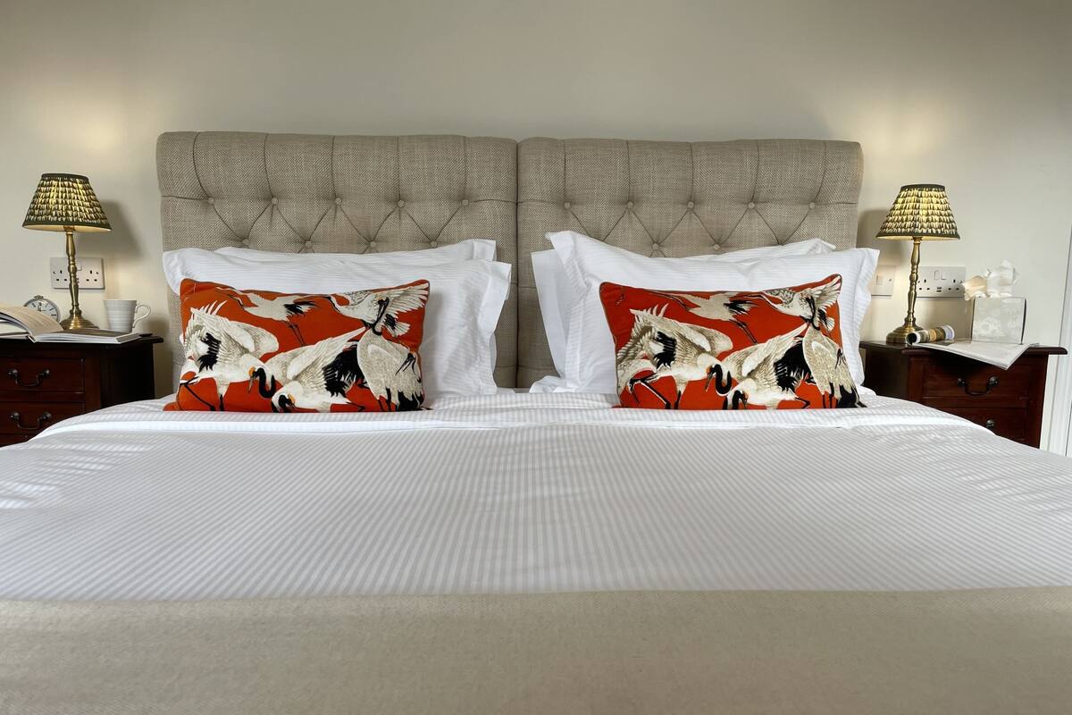 A neatly made bed with white linens, two decorative pillows with a bird pattern, a tufted headboard, and bedside lamps on wooden nightstands.
