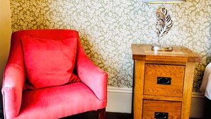 A red armchair, a wooden nightstand with drawers, and a lamp with a feather design.