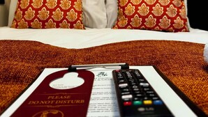 A hotel room with a bed, pillows, a remote control, a 'Please Do Not Disturb' sign, and a framed picture on the wall.