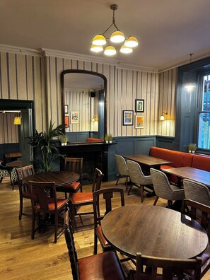 A dining area with striped wallpaper, a round wooden table, and a red bench. - George Hotel (Frome)
