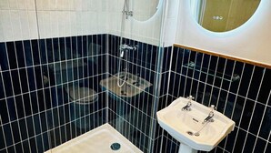 A modern bathroom with a glass-enclosed shower, a pedestal sink, and a round mirror.