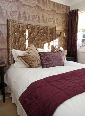 A neatly made bed with a headboard, a bedside lamp, and a window with curtains.