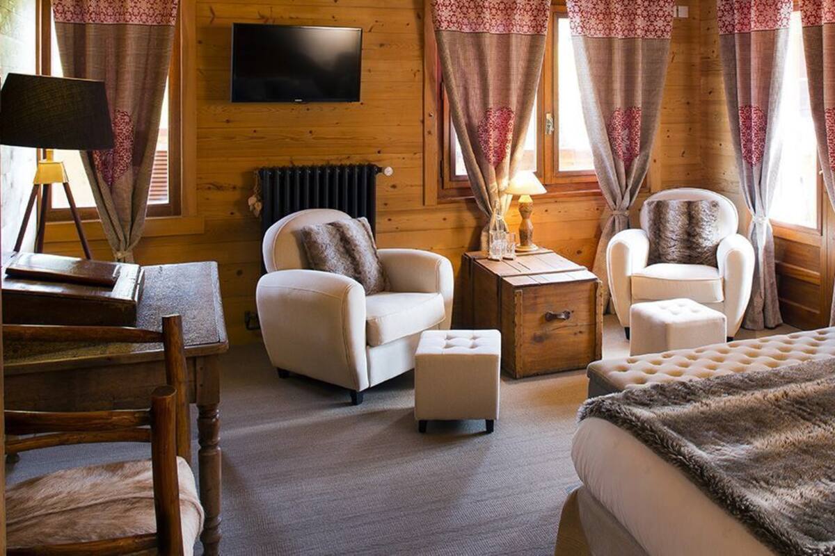 Una habitación acogedora con dos sillones, una mesita con una lámpara, una cama con una manta mullida y un televisor montado en la pared.