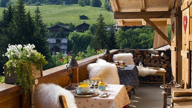 Una terraza de madera con una mesa dispuesta para comer, con vista a un paisaje montañoso.