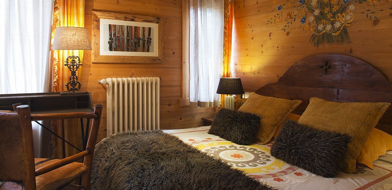 Una habitación acogedora de madera con una cama, dos lámparas, una silla y un cuadro en la pared.