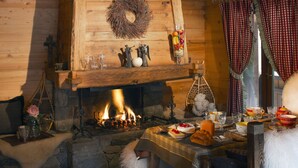 Una habitación acogedora con chimenea, paredes de madera, una mesa con comida y una ventana con cortinas escocesas.