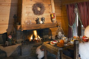 Cozy fireplace with a warm fire, dining area with table set and food, and traditional wooden walls.