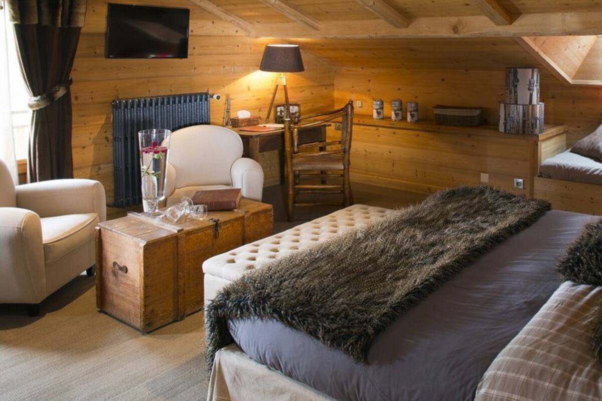 Un dormitorio rústico de cabaña con una cama grande, un tocador de madera, una silla y un escritorio con lámpara.
