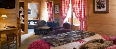 A cozy cabin-style room with a bed, a chair, a small table, and a television.
