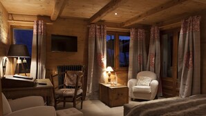 Acogedor cuarto de cabaña de madera con una cama, dos sillas, un escritorio con lámpara y vistas al exterior.