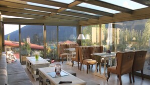 Une pièce spacieuse dotée d’un grand mur de verre offrant une vue sur les montagnes, et aménagée avec un canapé, des tables et des chaises.