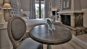 Une chambre à coucher avec un lit, une table ronde ornée d’un vase, une cheminée et un balcon avec des rideaux.