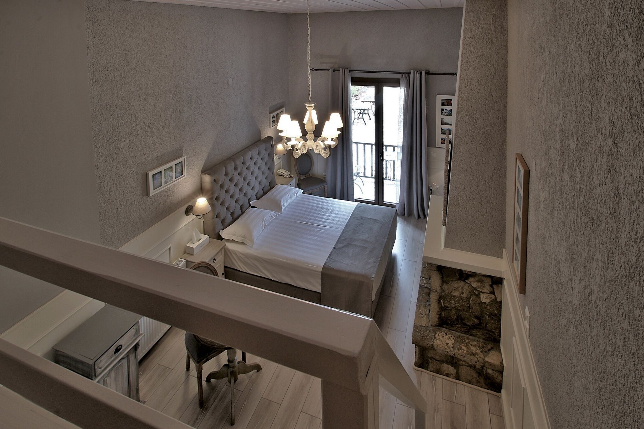 Quarto com uma cama grande, um candelabro, uma varanda com vista e uma parede de pedra.