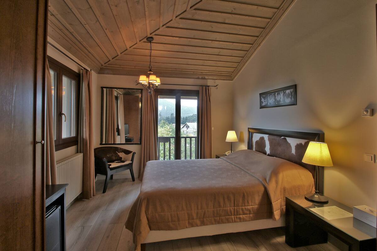 Un dormitorio con una cama grande, una silla, un escritorio, una lámpara y vistas al exterior.