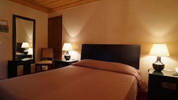 A hotel room with a bed, two bedside tables with lamps, a chair, a mirror, and a door.