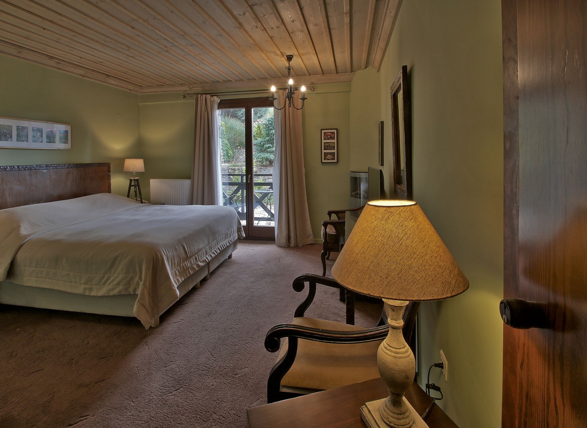 A bedroom with a bed, a desk with a lamp, a chair, a window with curtains, and a door.