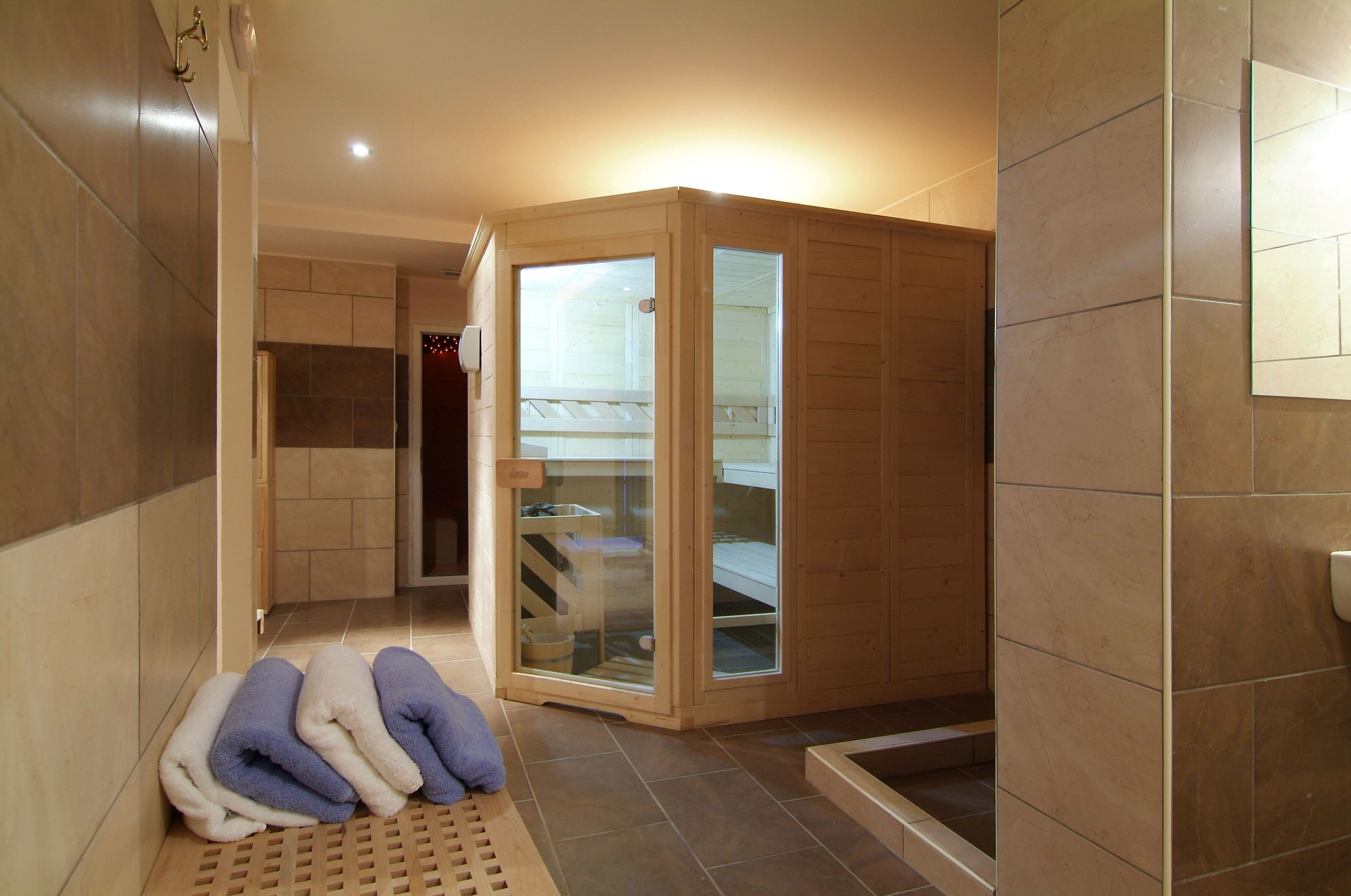 A sauna room with a glass door, wooden benches, and towels on the floor.