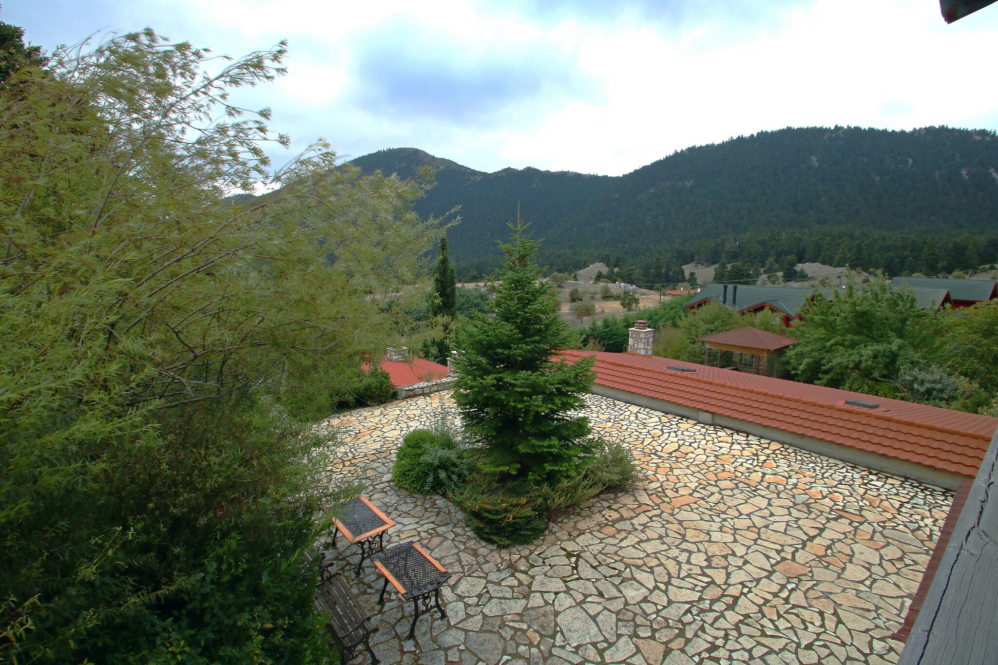 A stone patio with a small tree, a stone wall, and a view of a mountainous landscape.