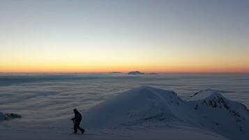 A person walking on a snow-covered mountain ridge with a view of the horizon and clouds below.