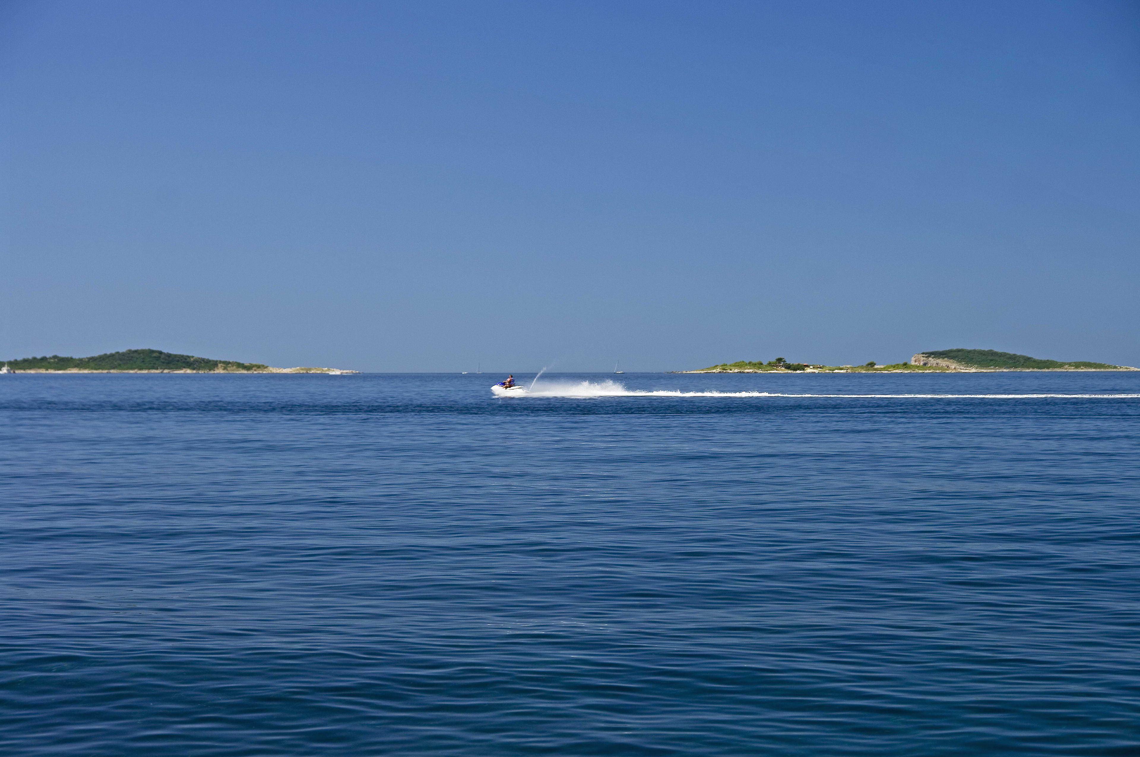 A boat speeding across a calm sea with distant green islands.