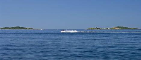 A boat speeding across a calm sea with distant green islands.