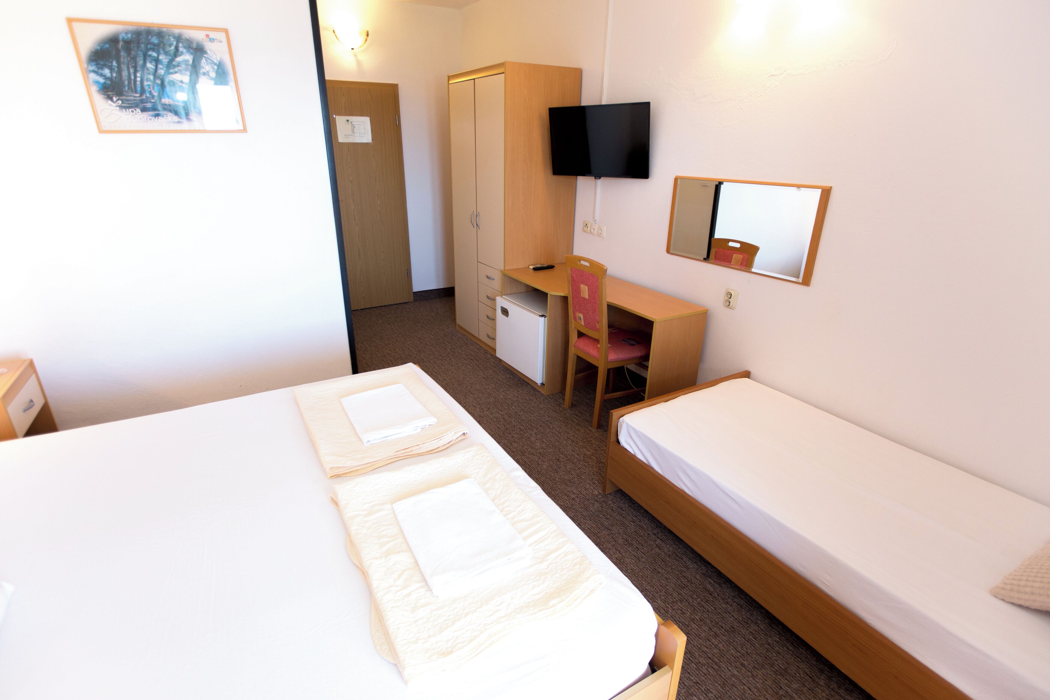 A hotel room with two beds, a desk, a chair, a television, and a wardrobe.