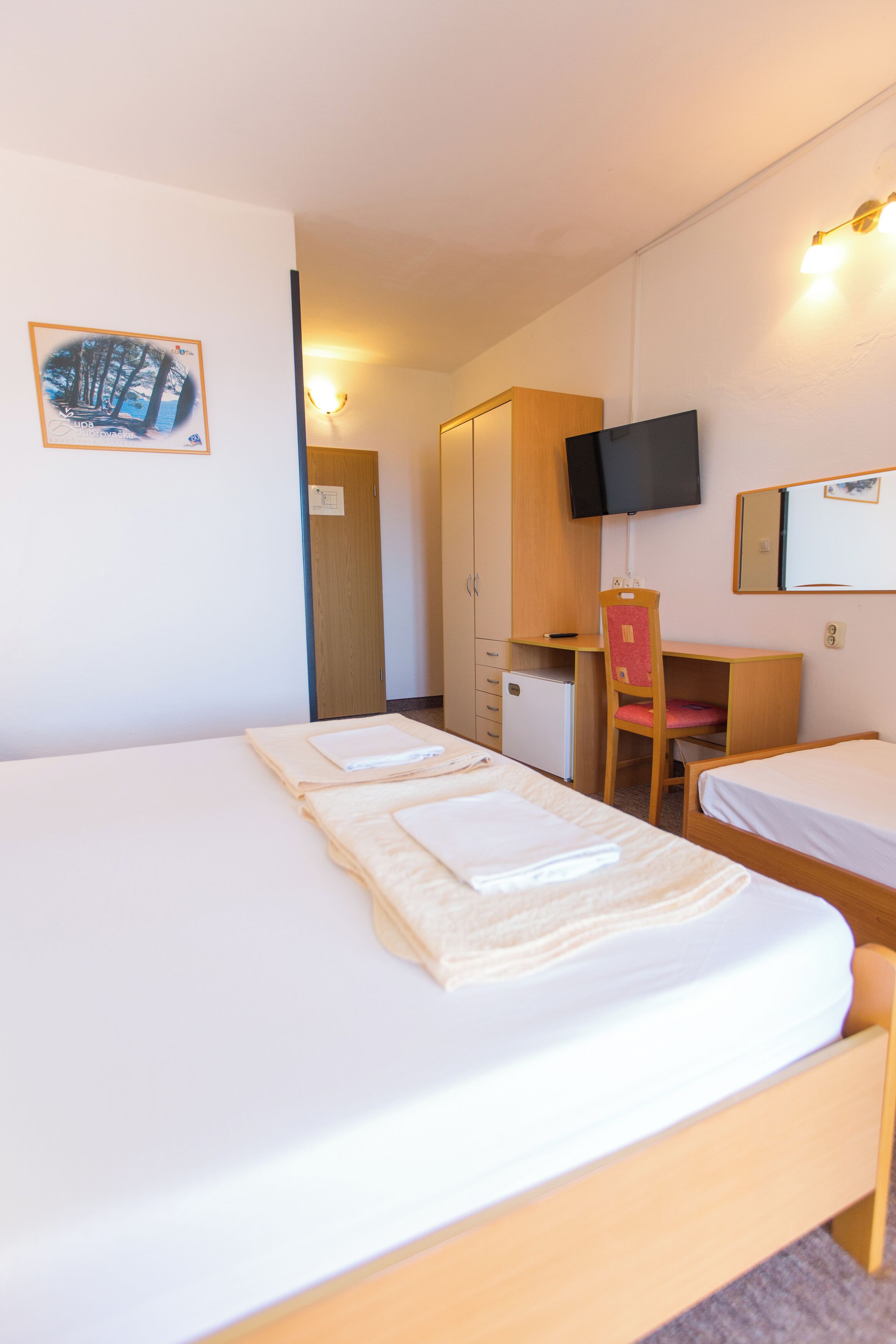 A hotel room with two beds, a desk, a chair, a television, and a wardrobe.