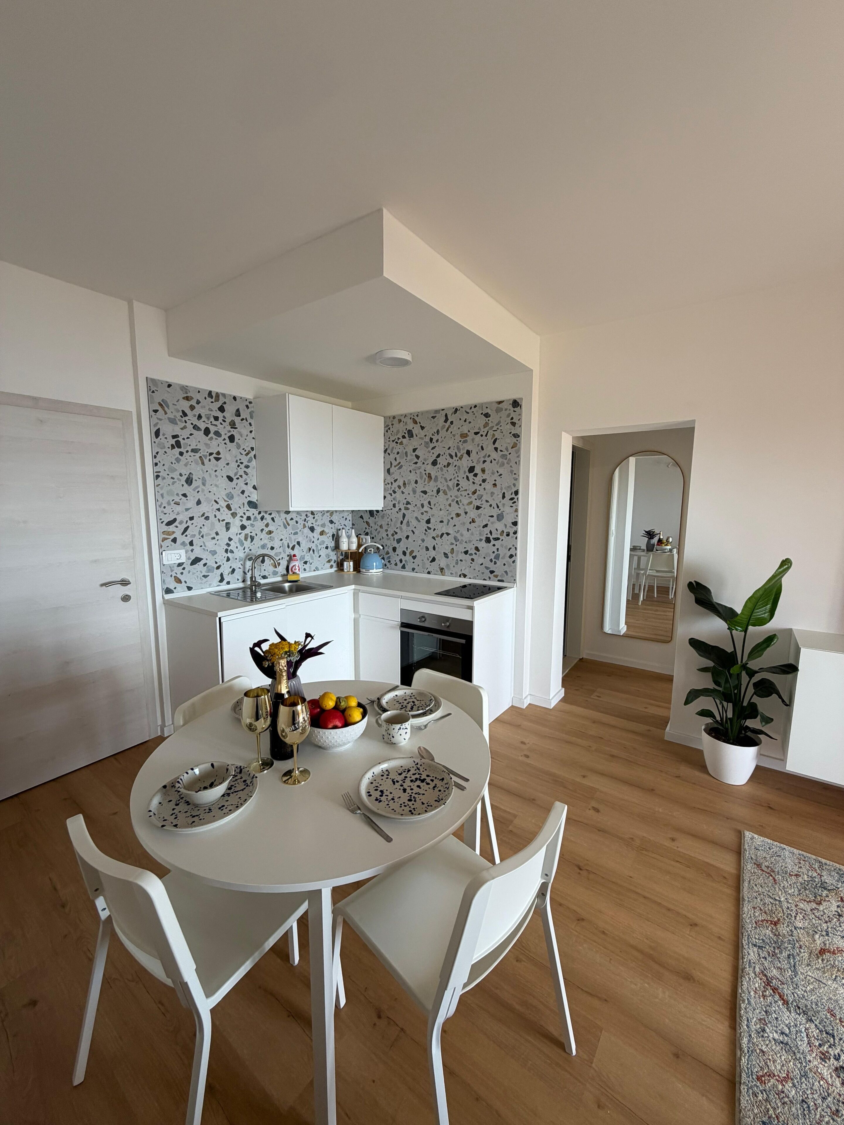 A modern kitchen with white cabinets, a terrazzo backsplash, and a dining area with a round table and white chairs.
