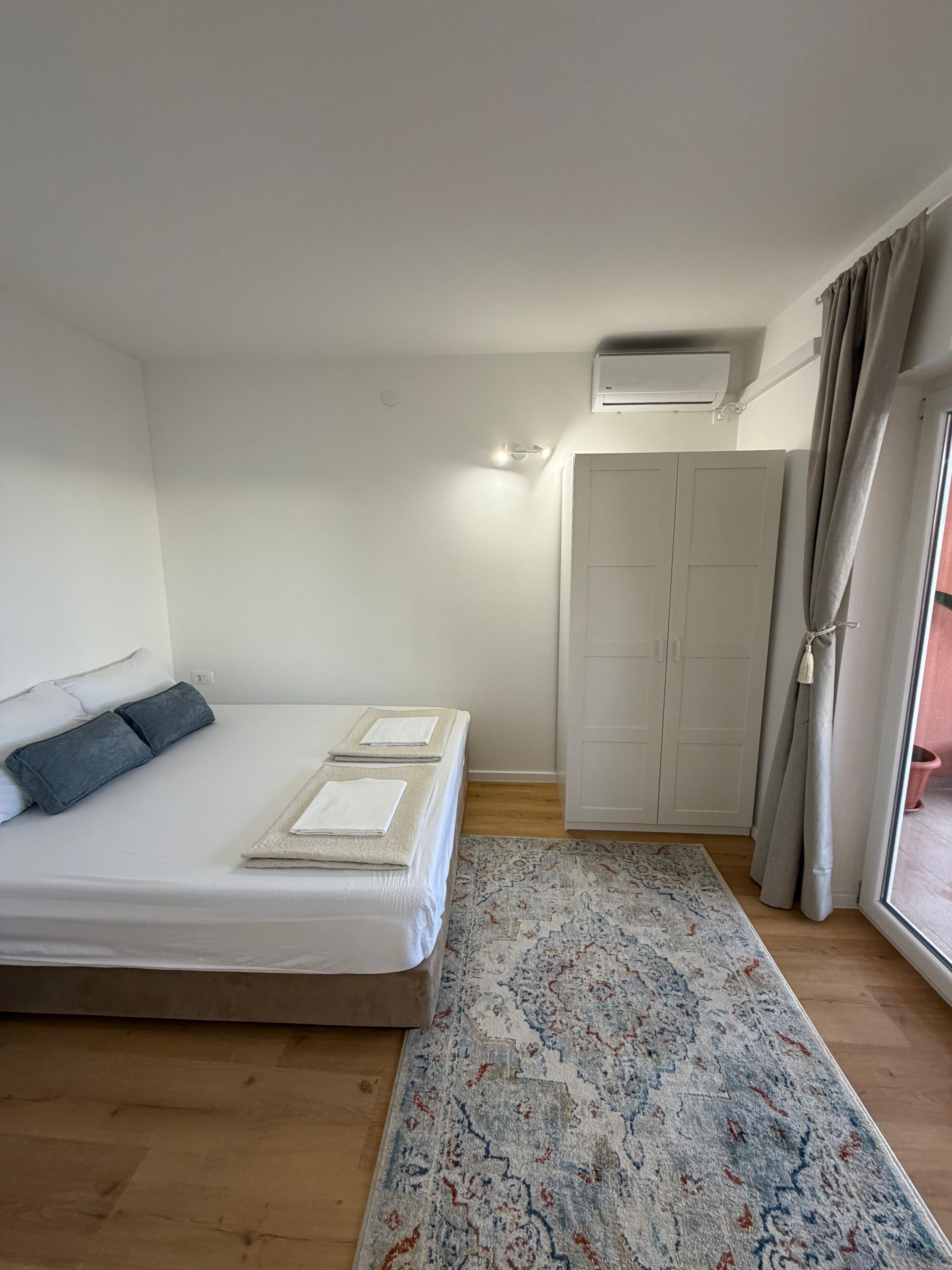 Une chambre à coucher comprenant un lit, une table de chevet, une armoire et une fenêtre avec des rideaux.