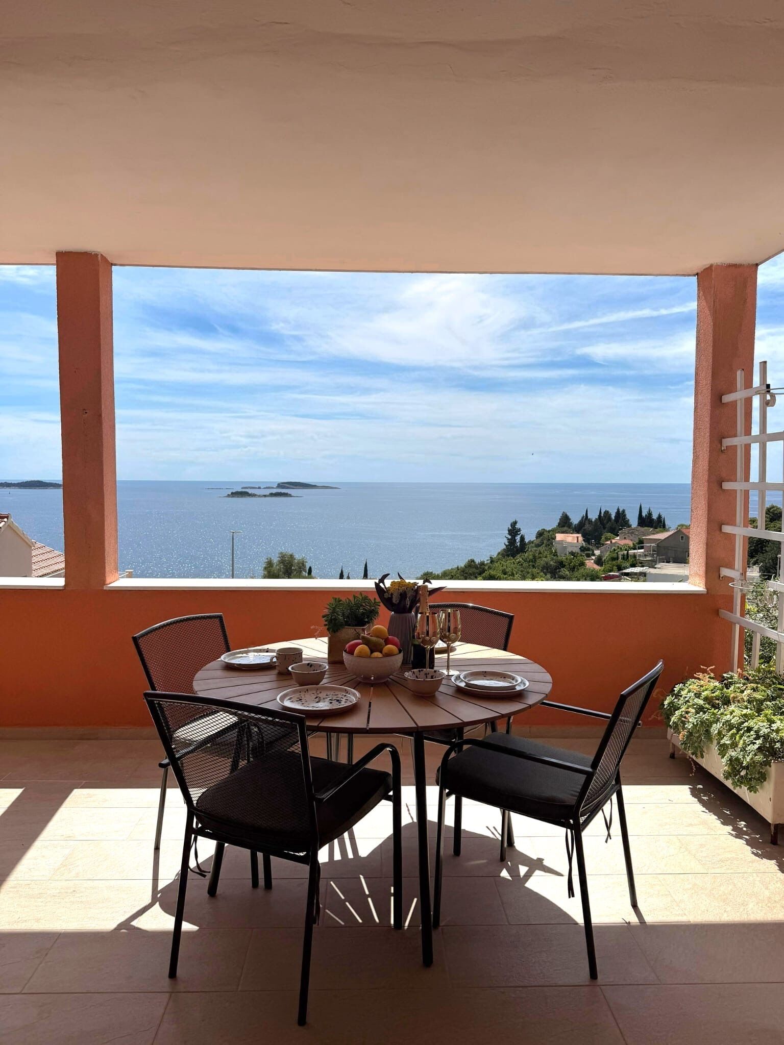 A terrace with a table set for two, overlooking a sea view.